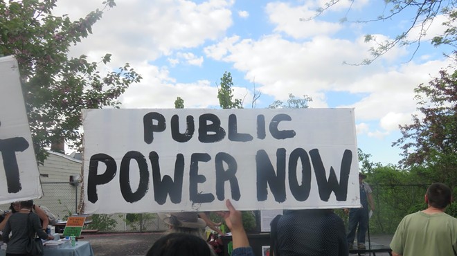 An activist holds up a hand-lettered sign that reads "Public Power Now."