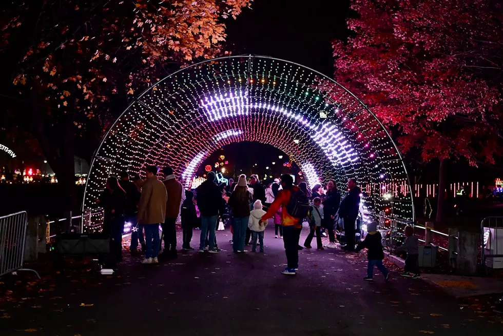 Families stroll through a colorful illuminated tunnel at Westchester&rsquo;s Winter Wonderland, surrounded by holiday lights and festive displays at night.